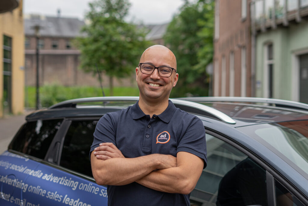 Marketingadviseur van Admeisters staat buiten voor een bedrijfsauto en lacht in de camera